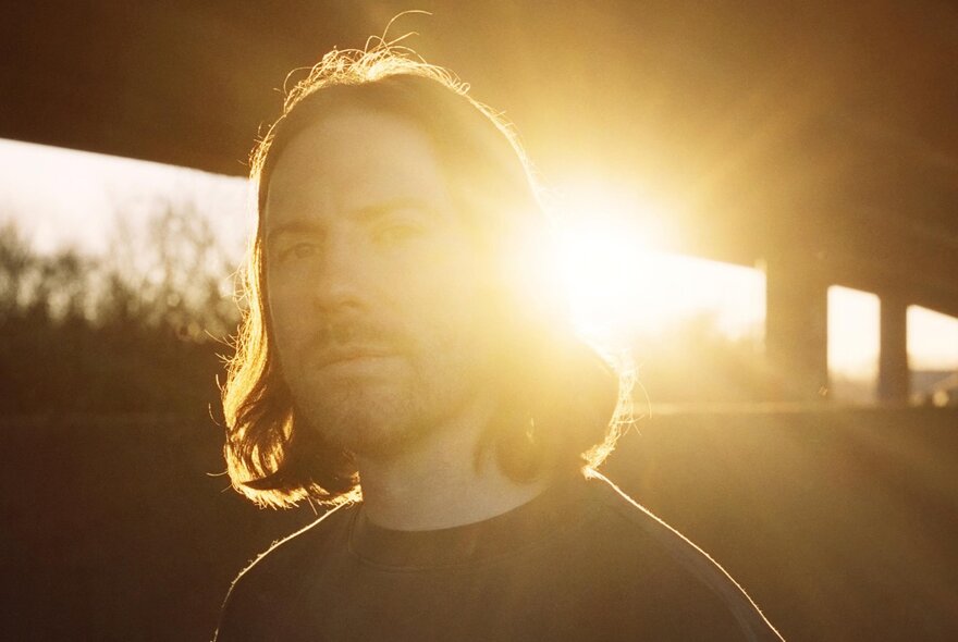 Man with shoulder-length hair and beard, sun shining through from behind. 
