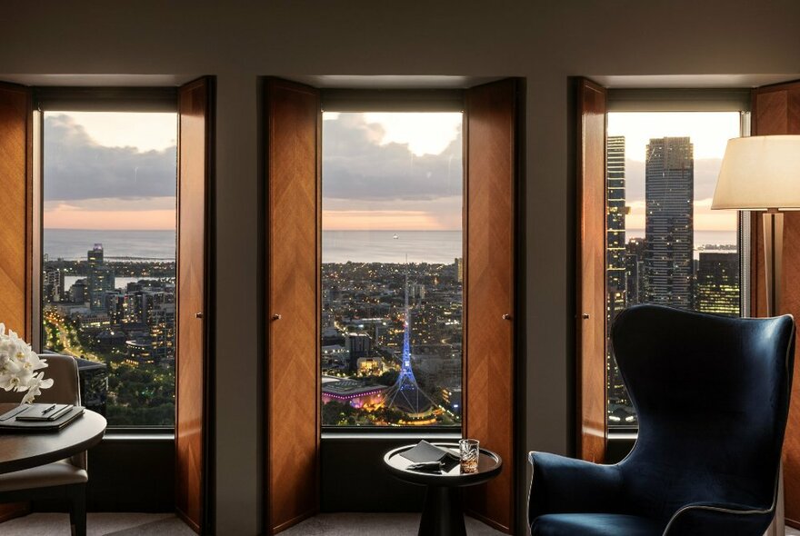 View out of a window of the Melbourne skyline from a room at the Sofitel on Collins, with a large armchair and small table positioned in front of the window.