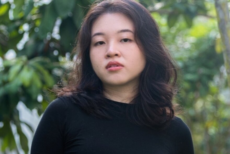 Portrait of a Singaporean woman wearing a black top, in front of a leafy green tree.