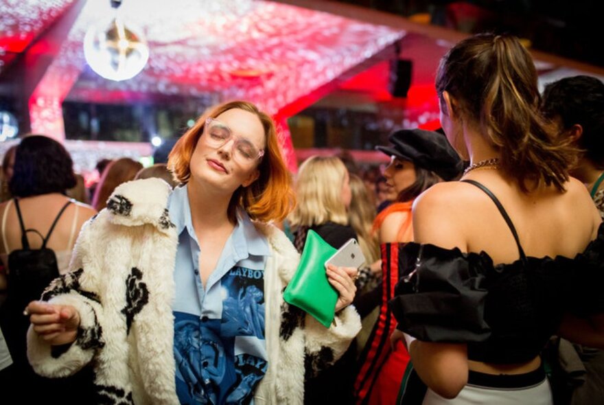 A woman with eyes closed, enjoying music in a nightclub environment.