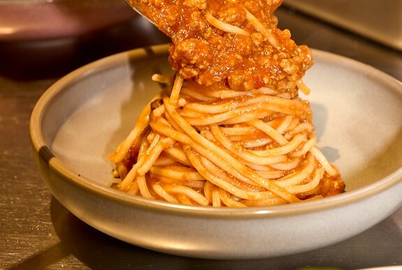 Bolognese sauce being poured onto spaghetti.