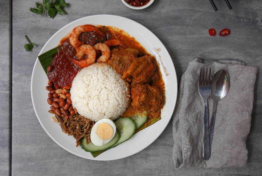 Rice and curry, prawns at top, half boiled egg and cucumber at bottom, in white bowl on grey surface.