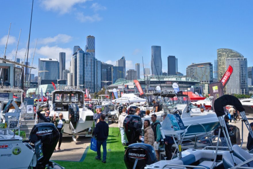 Boats on display at Docklands as part of the Melbourne Boat Show, with people walking around on the esplanade.