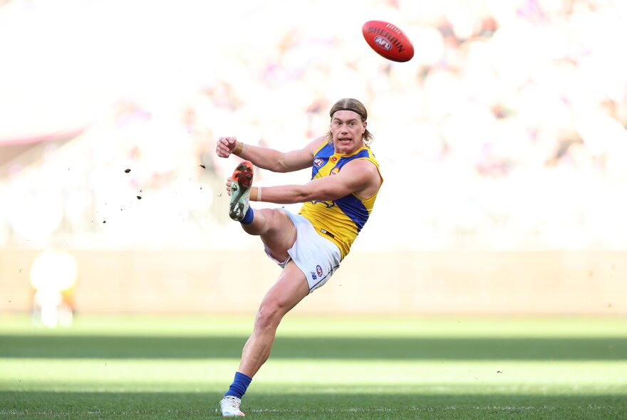 West Coast AFL football player kicking a red ball during a match.