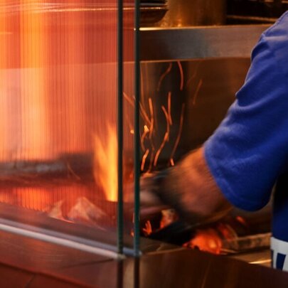 A chef in an open-concept kitchen at a restaurant with a fiery BBQ grill.