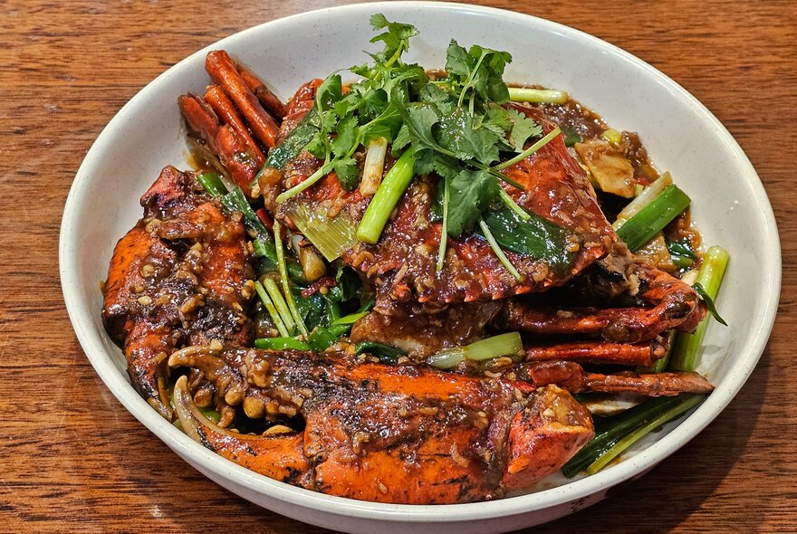 A Malaysian fried crab on a bed of stir-fried vegetables in a bowl.