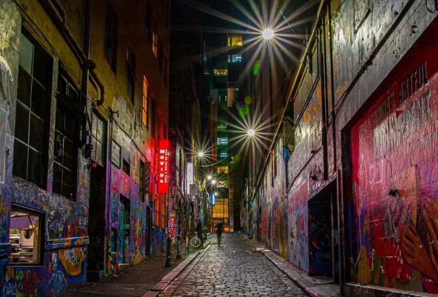 A person walking down graffiti-covered Hosier Lane at night with glowing lights.