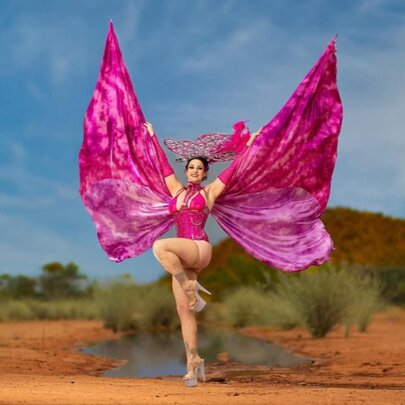Performer in a desert setting, dancing on one leg with butterfly wing costume.