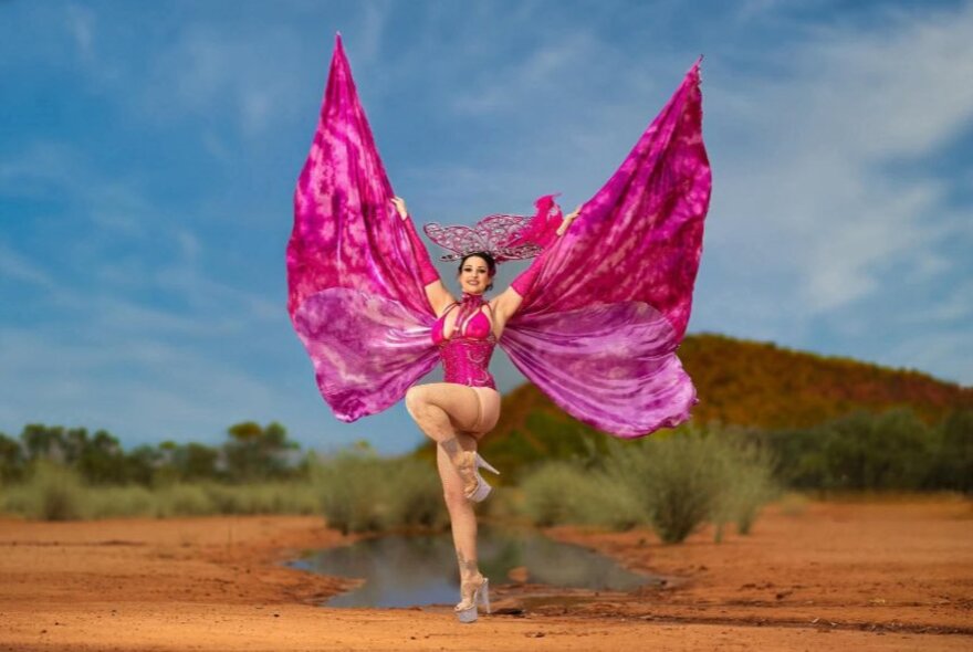 Performer in a desert setting, dancing on one leg with butterfly wing costume.