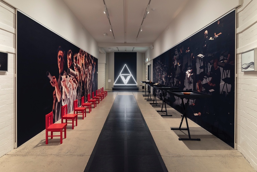 Installation of an exhibition at Grainger Museum with red chairs lined up against one wall facing a row of percussive instruments on black stands on the opposite wall.