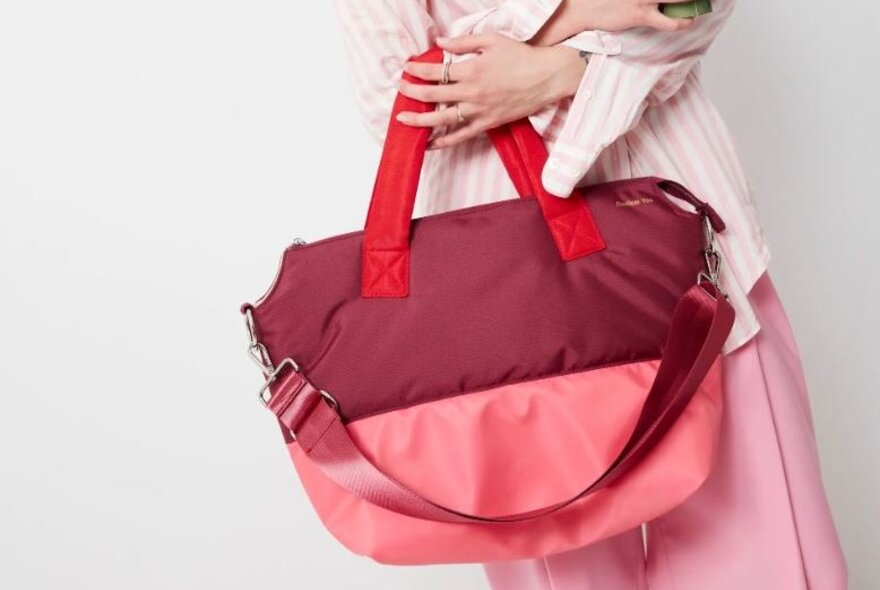 A person is carrying a pink and burgundy bag.