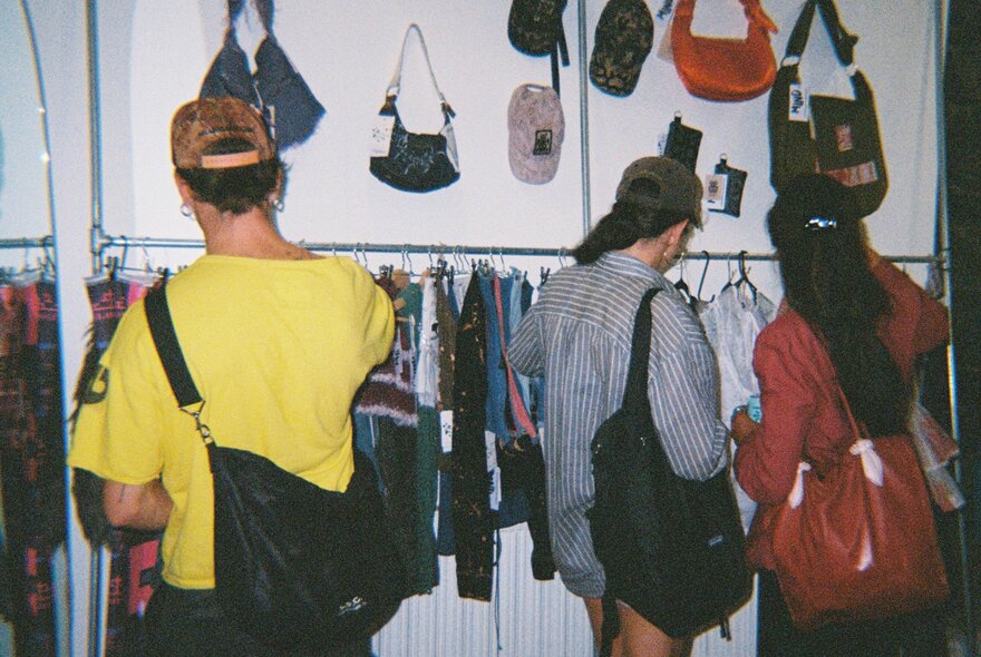 Three people shopping in a circular fashion pop up store, with racks of clothing and bags hanging on the wall.
