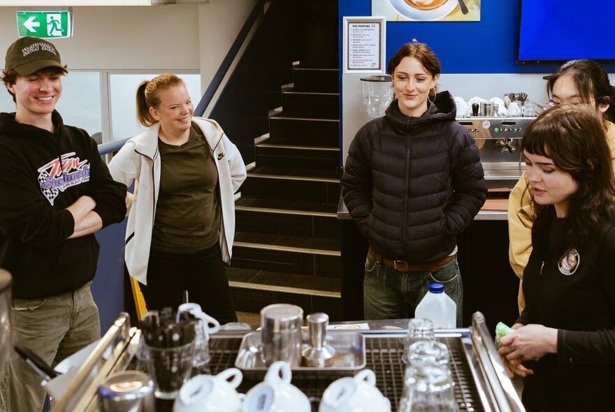 Five people looking relaxed learning to use an espresso machine. 