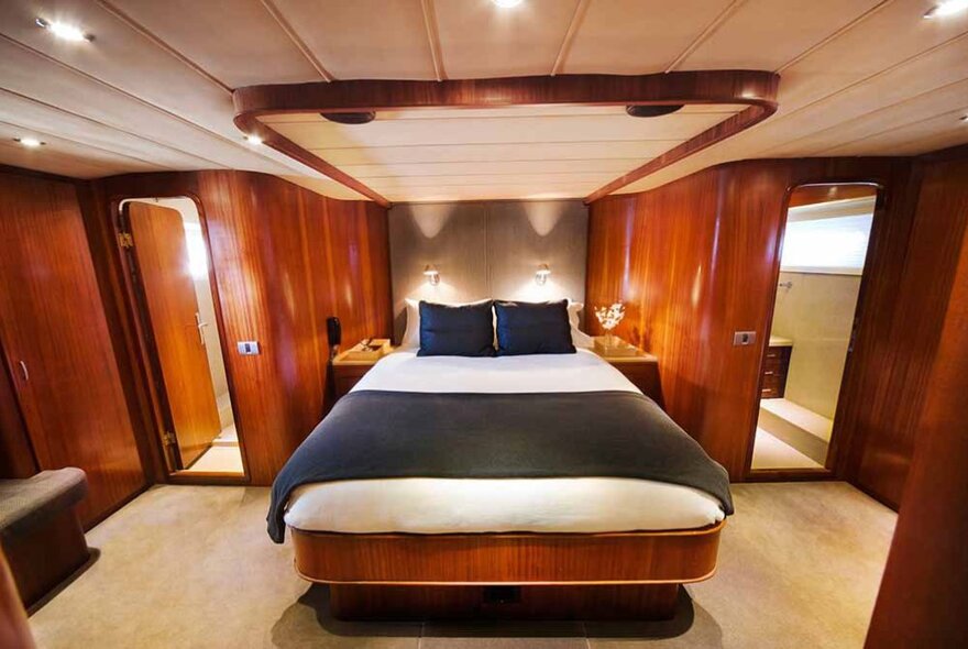 The luxury cabin of a superyacht, with queen sized bed and gleaming timber walls.