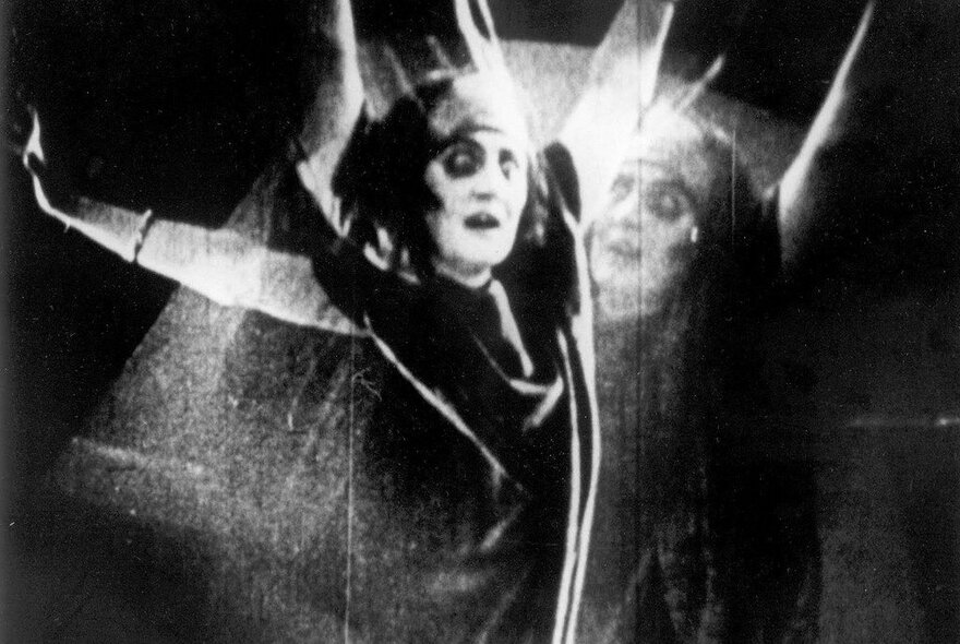 A black and white still from the 1928 French horror film, The Fall of the House of Usher, showing a blurred image of a woman with her arms outstretched and fearful eyes.