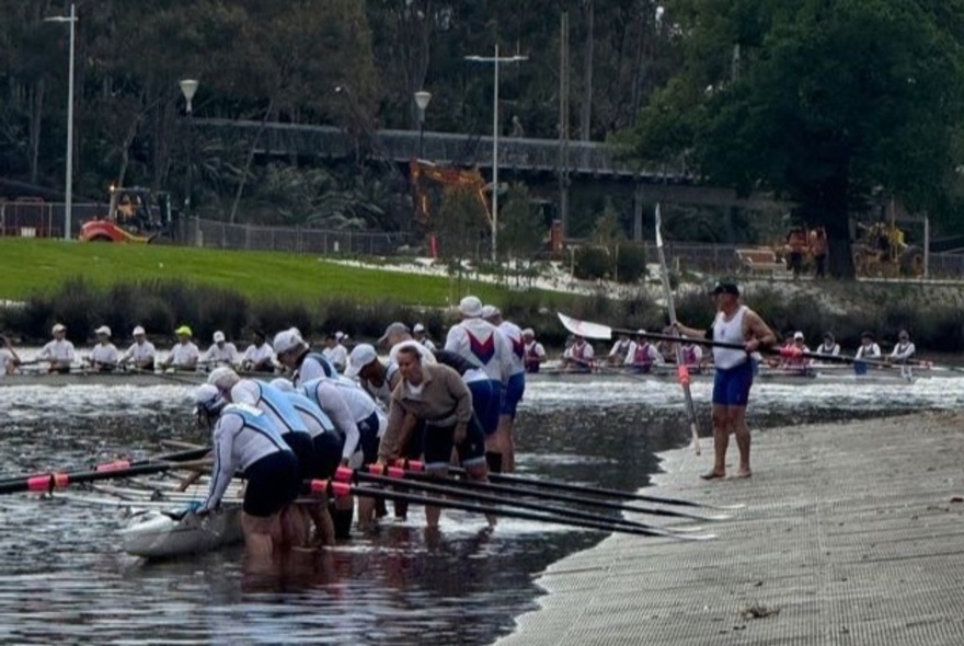 A rowing team preparing to depart from the riverbank.