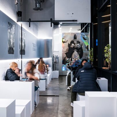 Interior of a cold looking, minimalist bar with people seated at white block booths. 