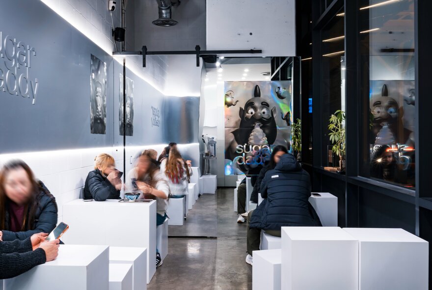 Interior of a cold looking, minimalist bar with people seated at white block booths. 