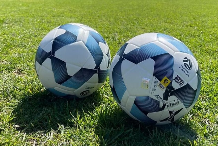 Two soccer balls on a grass pitch.