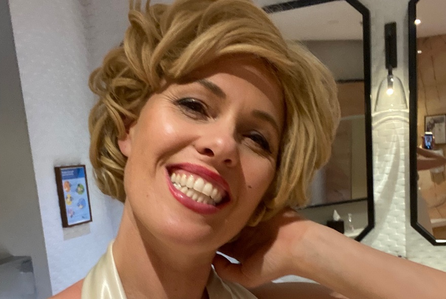 Marilyn Monroe tribute performer wearing blonde wig and makeup, smiling broadly.