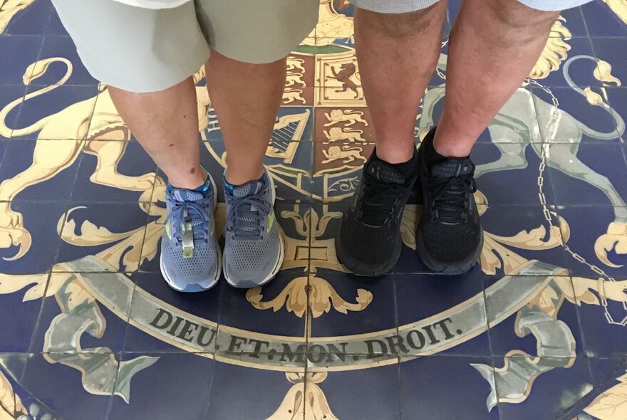 The feet of two people on a walking tour, standing on a tiled floor.