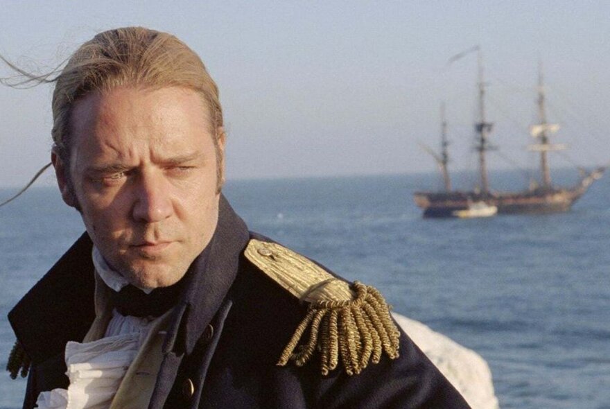 A still from the movie, Master and Commander, of a seafaring Naval captain with a tall ship and the ocean in the background.