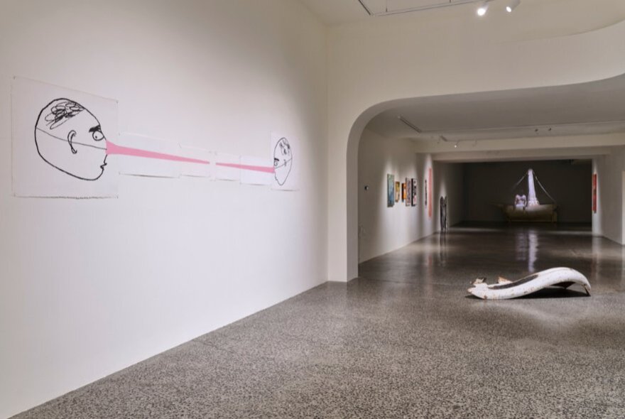 Installation view inside a gallery, with a line drawing on the white wall and a sculpture in the middle distance on the polished concrete floor.