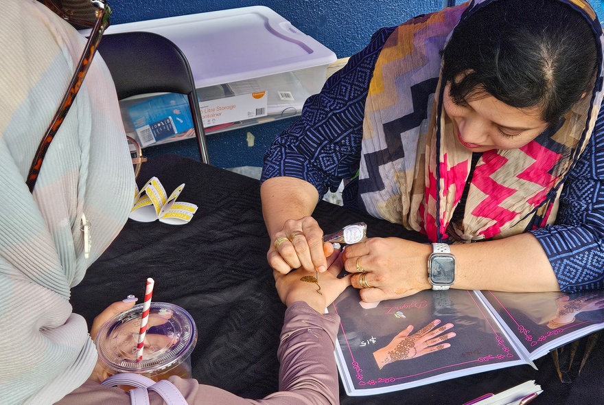 Woman drawing on a woman's hand with ink, following traditional designs.