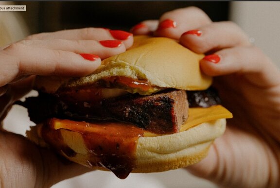 Hands with red nailpolish holding a brisket sandwich.