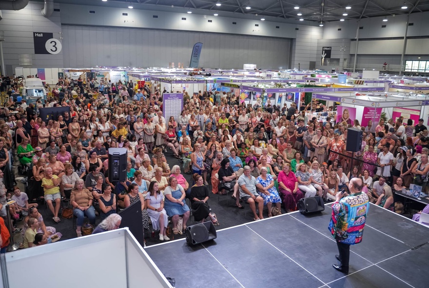 A crowded main stage event at the MindBodySpirit Festival, held inside a large convention centre.