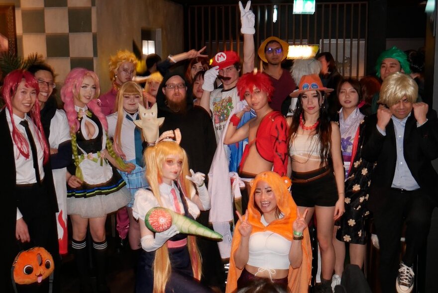 A large group of people dressed in cosplay, smiling and posing for the camera, inside a foyer.