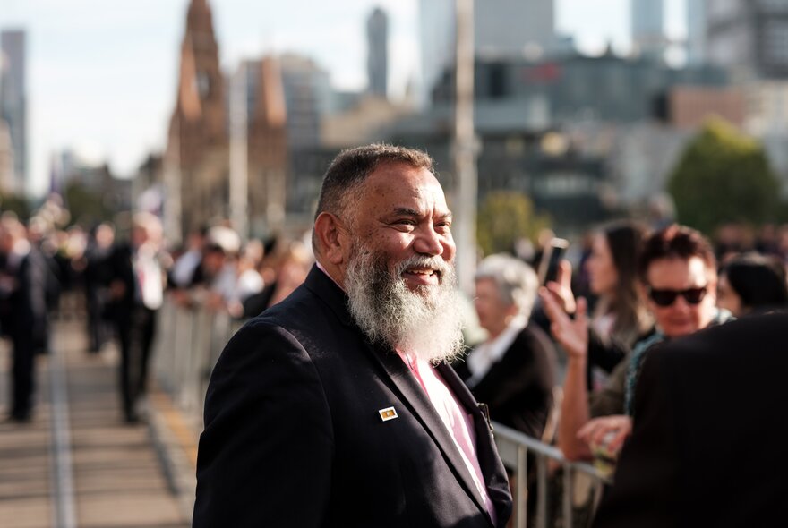A retired serviceman with a beard smiling at a crowd of people while marching in the ANZAC Day Commemoration March.