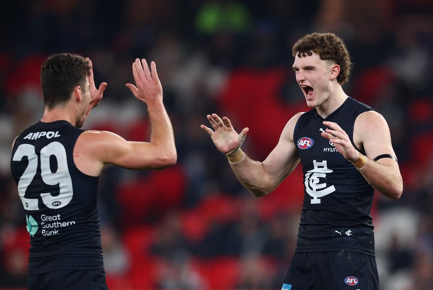 Two Carlton football players meet to clap hands in the middle of the football field. 