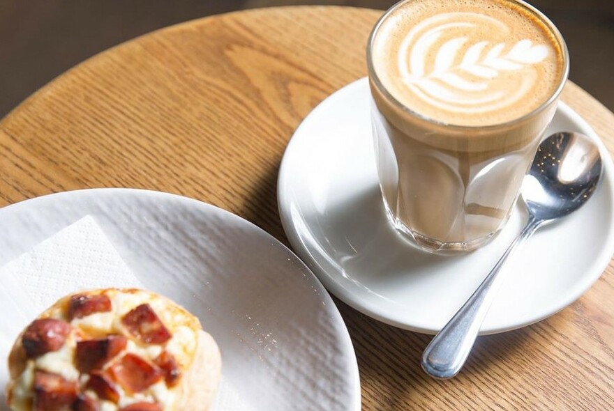 Table with a coffee in a glass and a side plate of a muffin.