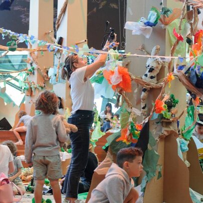 Families working with paper craftworks hanging from ropes in an indoor space.