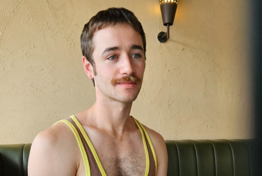 A man in a low-cut singlet staring wistfully. 
