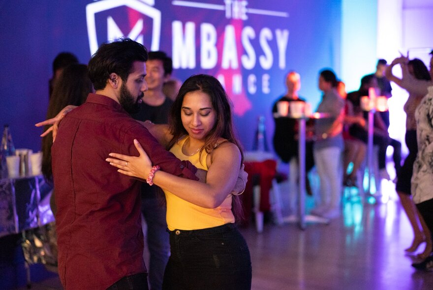 A couple dancing arm in arm on a dance floor with purple lights.