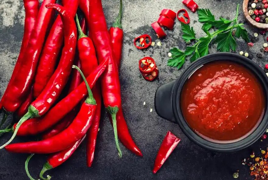 Fresh and sliced red chilli peppers next to a pot of sauce.