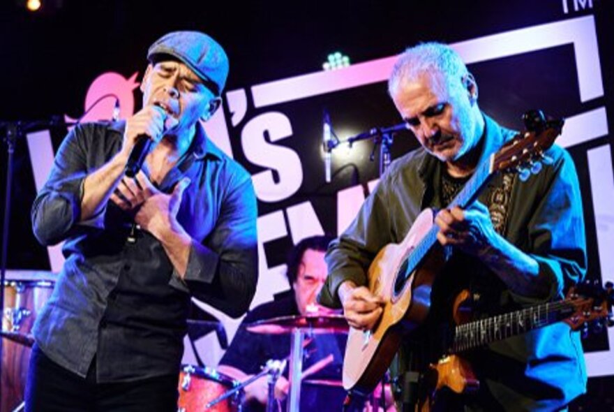 A band of male musicians on stage at Bird's Basement, playing instruments and one of them singing.