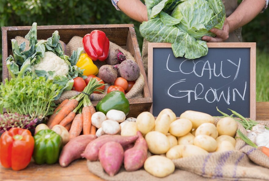 A vegetable stall at an outdoor market with a table of fresh vegetables and a small blackboard sign with the words LOCALLY GROWN written in chalk on the board.