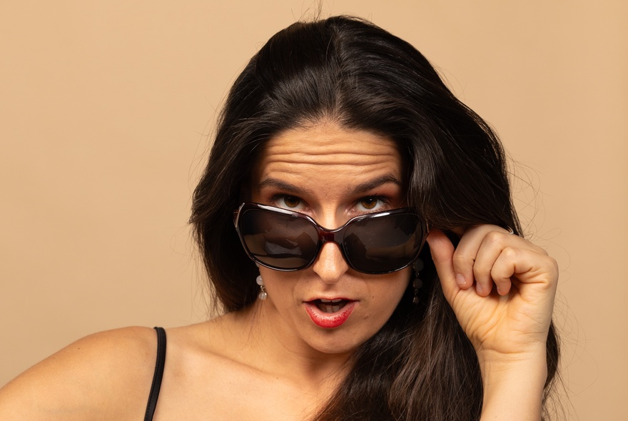 A woman peering over the top of a pair of dark sunglasses that she is wearing on her face.