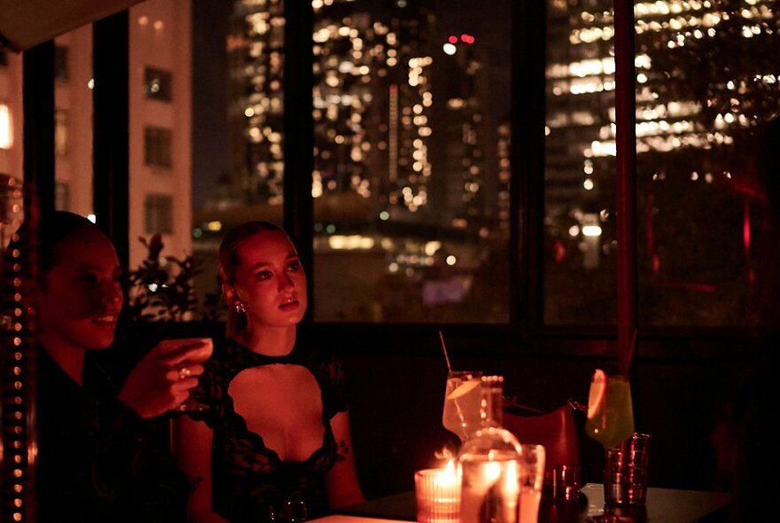 A dark, candlelit bar with a well dressed woman and man having a cocktail and CBD lights visible behind them. 