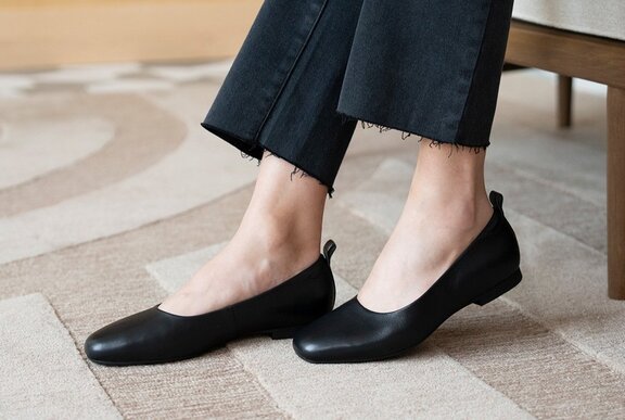Feet wearing a pair ballerina flats in black leather.