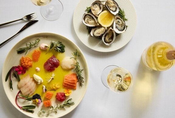 A top-down view of a dining table with two plates of food and glasses of white wine.