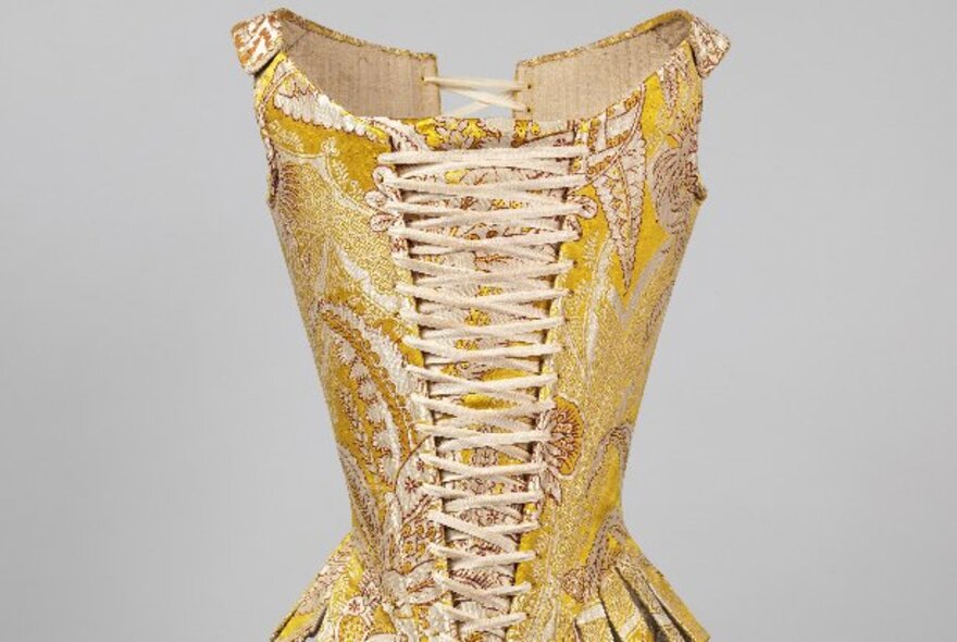 An antique corset with white webbing and yellow paisely fabric.