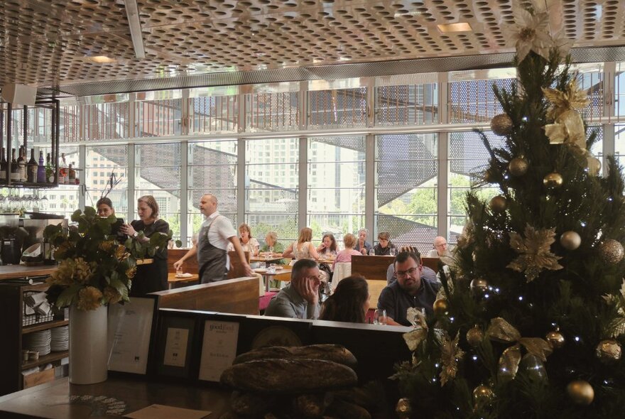 Staff beside patrons eating and drinking, surrounded by high floor to ceiling windows.