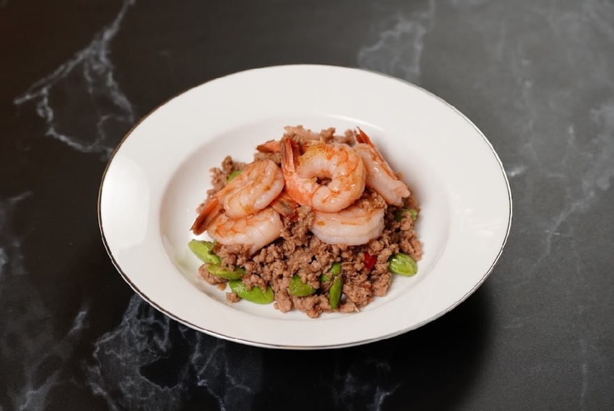 A white dish of stir-fried prawns on a table. 