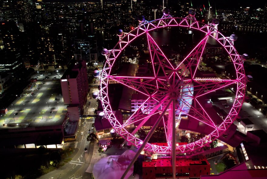 Melbourne Observation wheel lit up with pink lights at night.