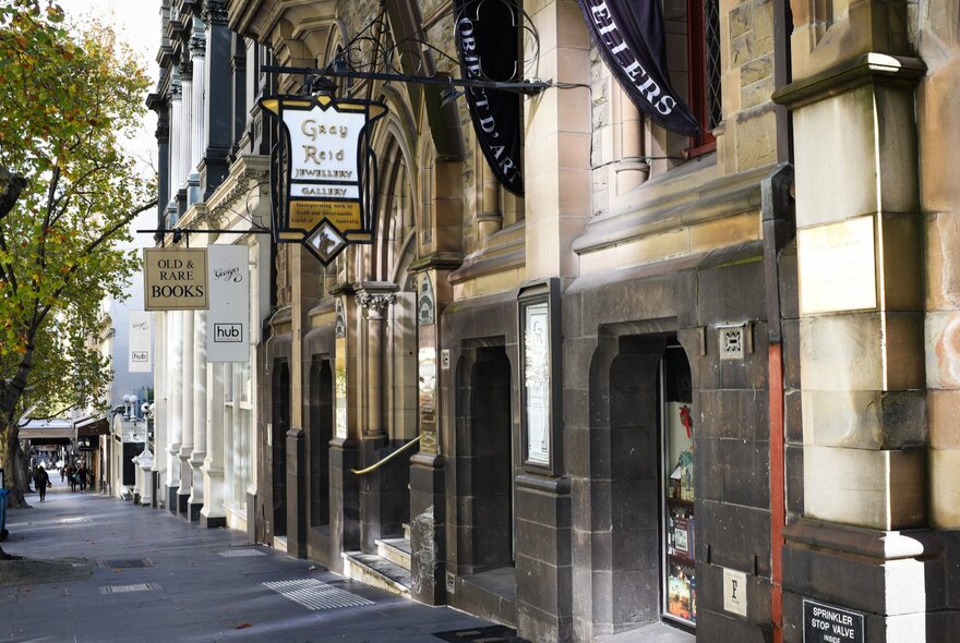A heritage building with a stone exterior and shop signs hanging on wrought iron. 