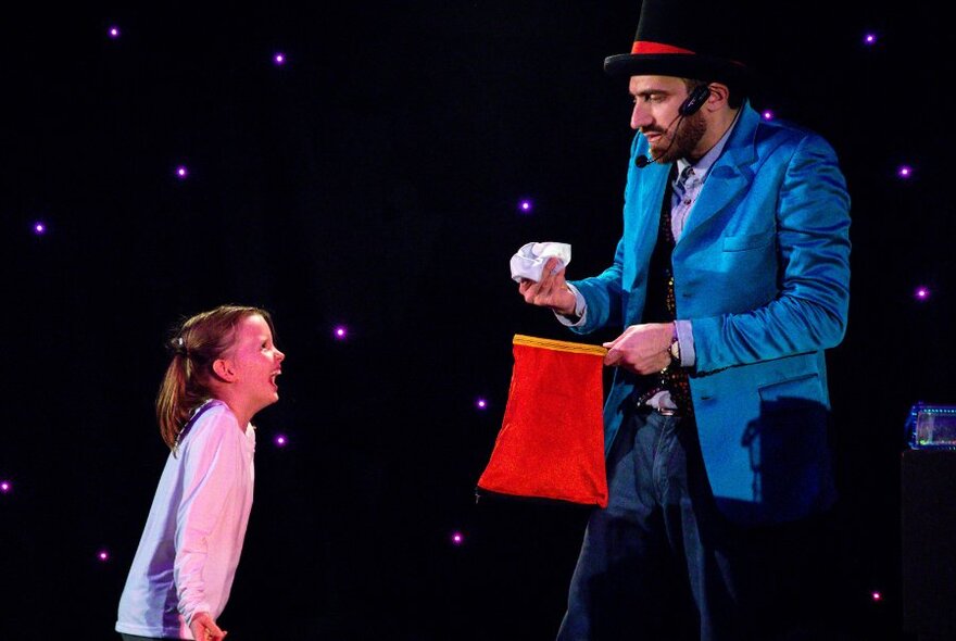 The Great Armando performing an illusion on stage with a child looking on and laughing.